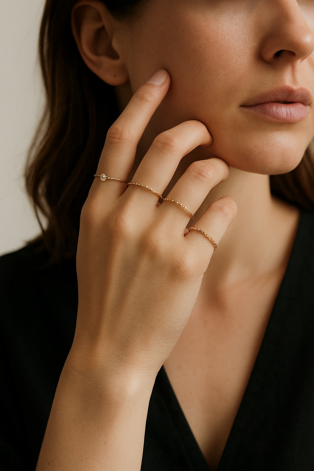 Close-up of a woman's hand with gold rings on her fingers, touching her face.