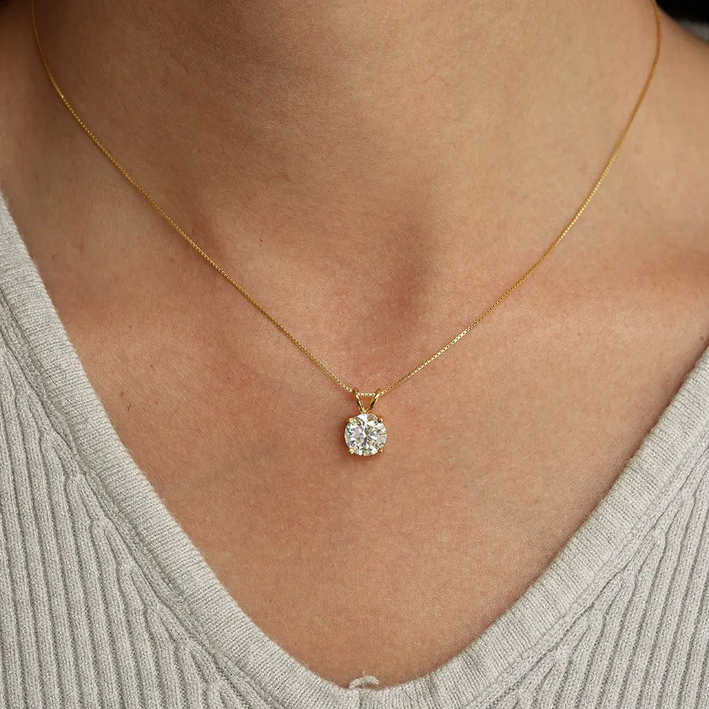 Gold necklace with a diamond pendant on a person wearing a light gray top.