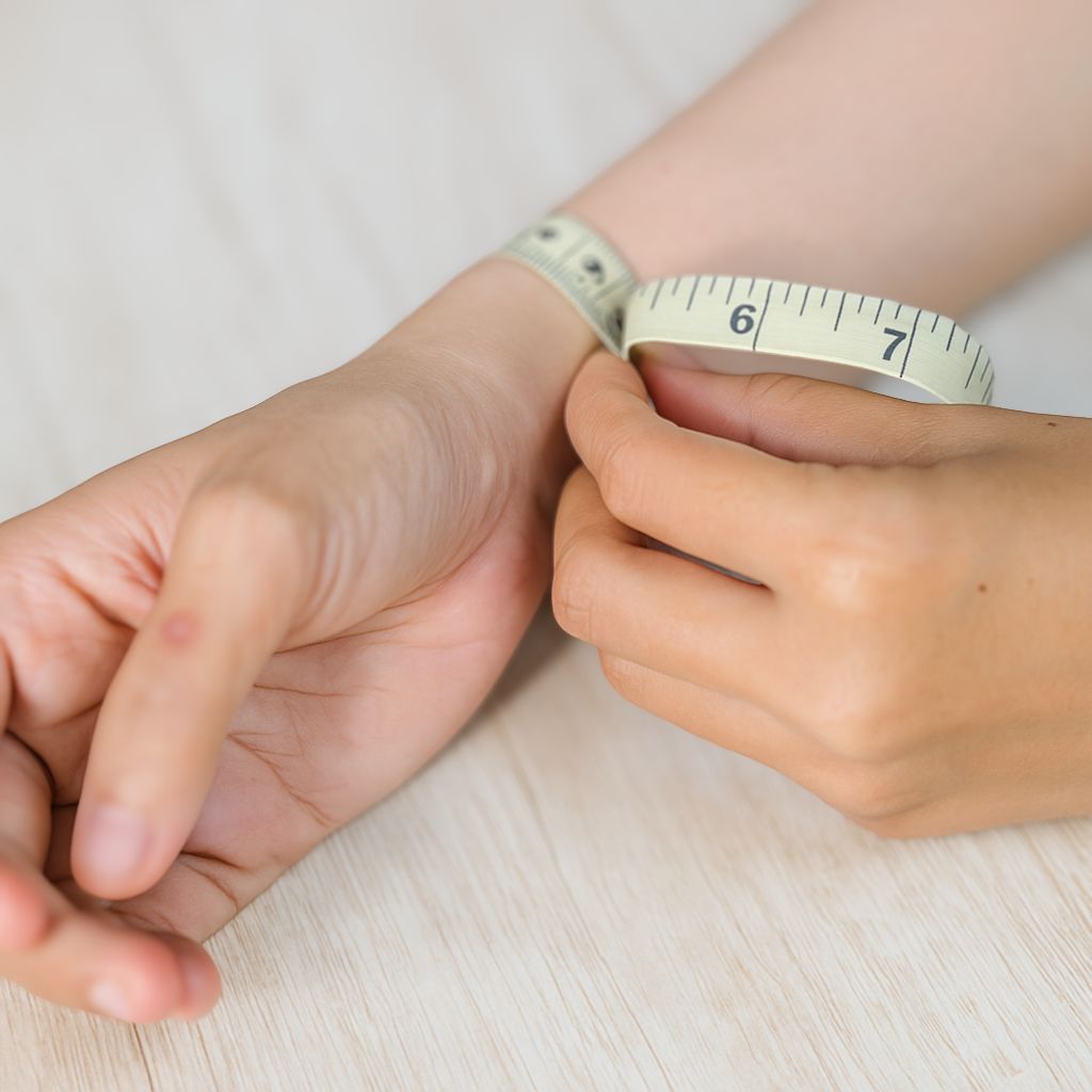 Close-up of hands measuring a wrist with a tape measure on a light background