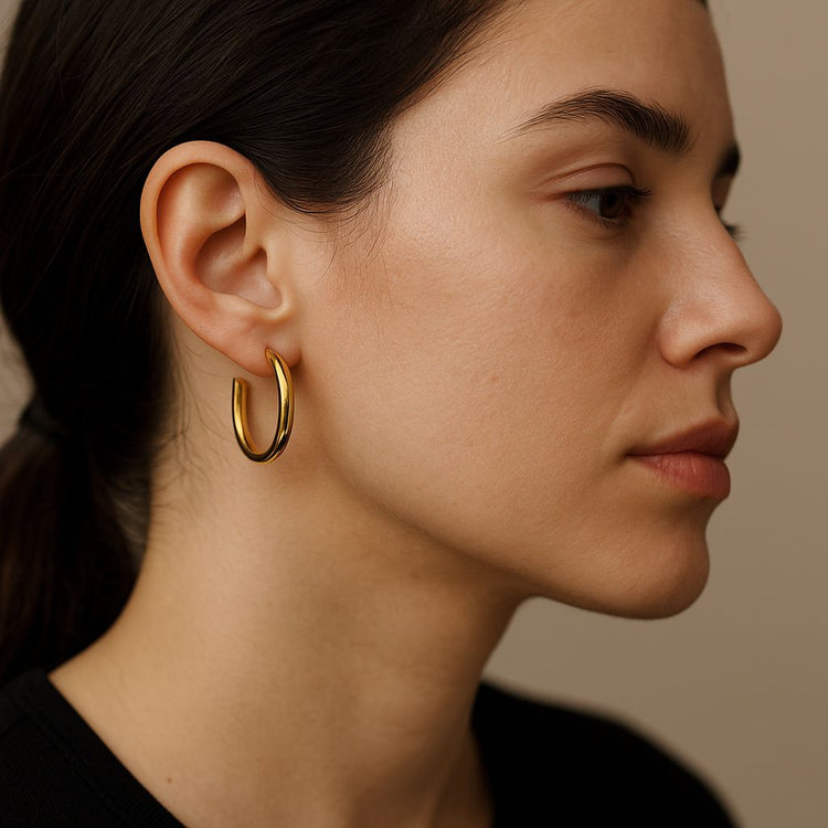 Close-up of a woman wearing medium gold hoop earrings against a neutral background