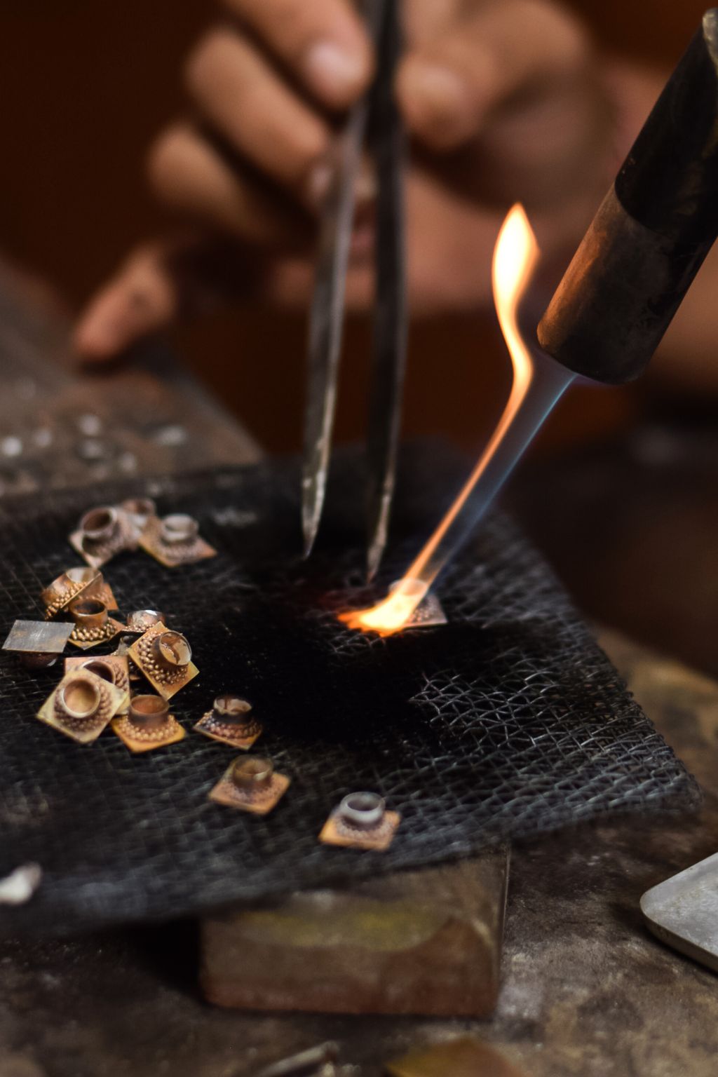Person using a torch to melt a small  silver on a dark surface.