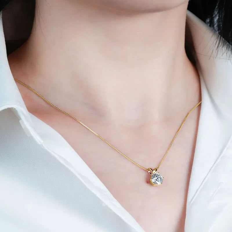 Gold necklace with a diamond pendant worn by a person in a white shirt.