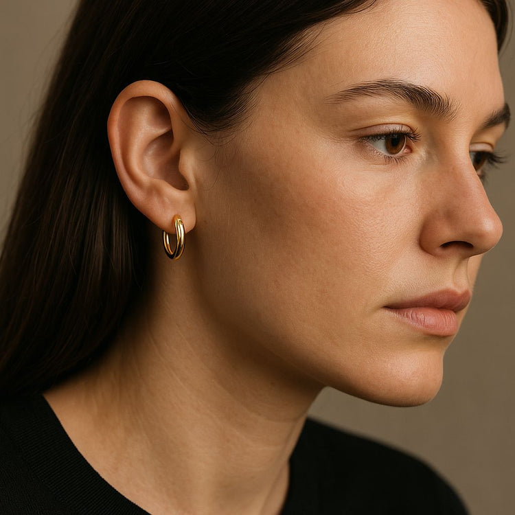 Close-up of a woman wearing a small gold hoop earrings against a neutral background