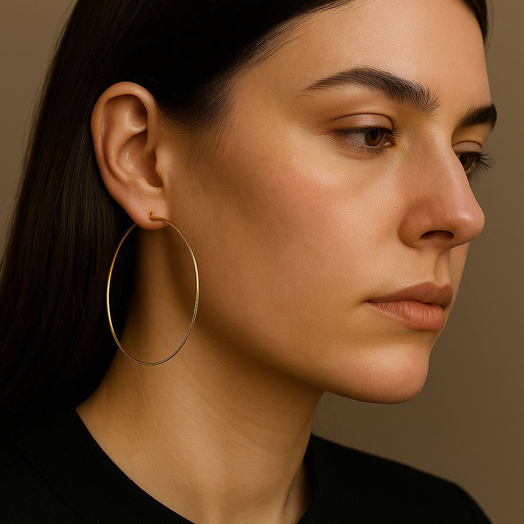 Close-up of a woman wearing an oversized gold hoop earrings against a neutral background