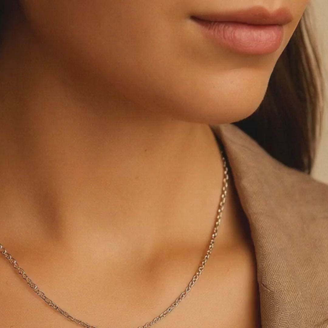 Close-up of a person wearing a silver necklace with a beige blazer.